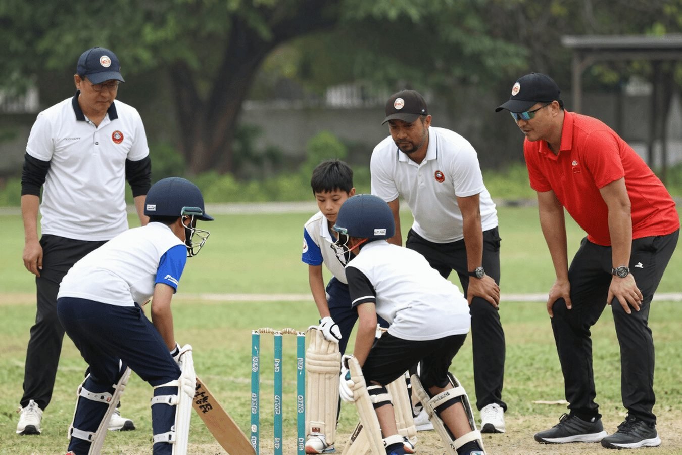Young players batting and fielding while coaches supervise a drill.